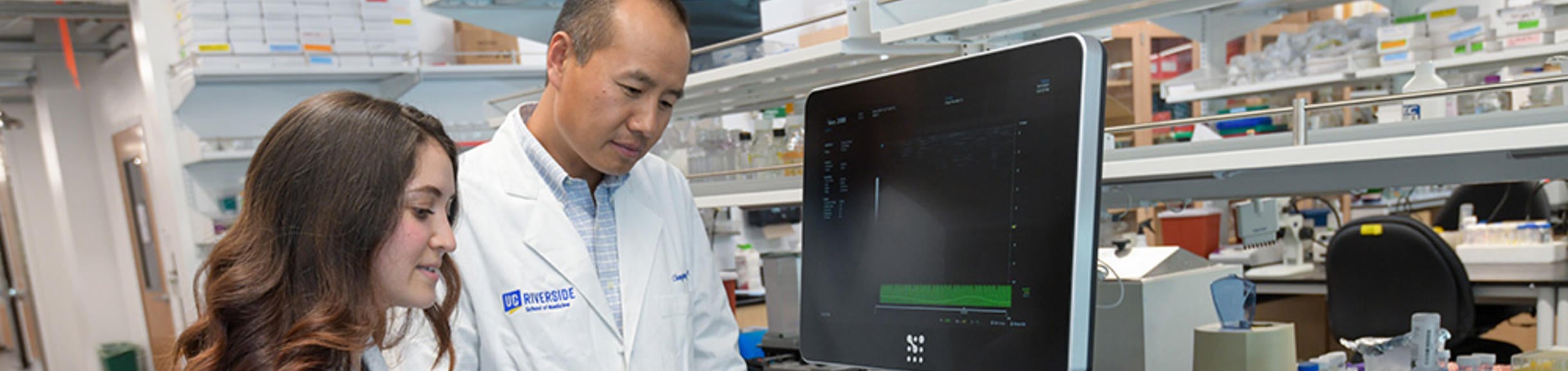 a faculty member and graduate student looking at data on a device screen in a lab