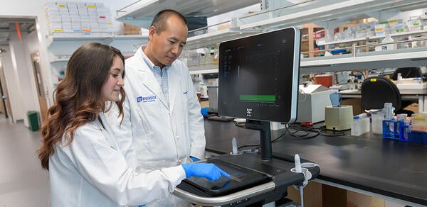 a faculty member and graduate student looking at data on a device screen in a lab