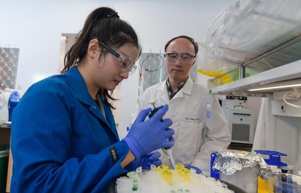 Research assistant supervised by a Researcher prepares a sample for processing.